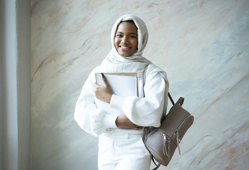 a woman wearing a white outfit holding a folder and a backpack